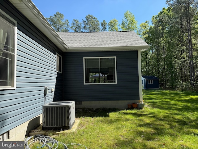 14273 Brandy Ln, Georgetown, DE 19947 - view of side of property with central air condition unit, a yard, an outbuilding, roof with shingles, and a storage shed