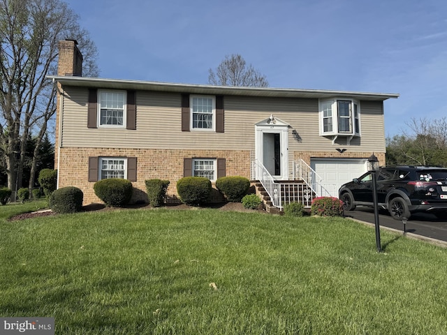 raised ranch with a front lawn, a chimney, a garage, and brick siding