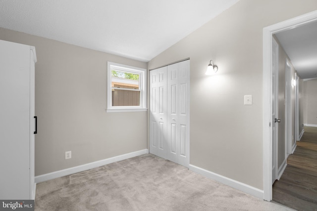unfurnished bedroom featuring baseboards, carpet floors, lofted ceiling, and a closet