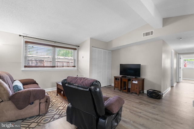 living area featuring lofted ceiling with beams, a textured ceiling, baseboards, wood finished floors, and visible vents
