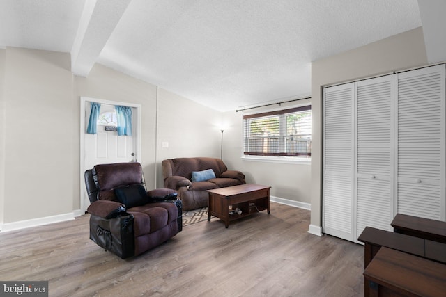 living area with light wood-type flooring, lofted ceiling with beams, baseboards, and a textured ceiling