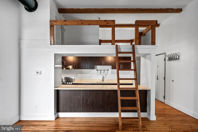 kitchen with dark brown cabinetry, wood finished floors, a sink, light countertops, and baseboards