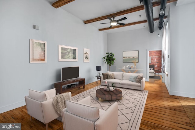 living area with beam ceiling, wood-type flooring, a ceiling fan, baseboards, and a towering ceiling