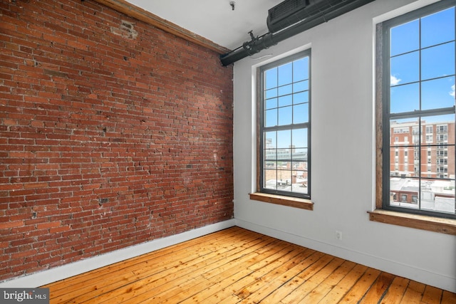 spare room featuring baseboards, wood-type flooring, and brick wall