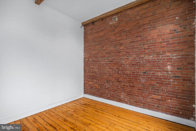 unfurnished room with baseboards, wood-type flooring, and brick wall