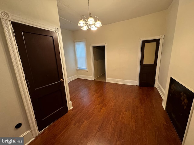 unfurnished dining area with a notable chandelier, baseboards, and dark wood-type flooring