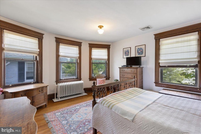 bedroom with light wood-style floors, radiator, and visible vents