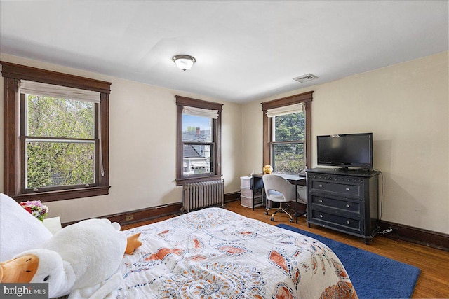 bedroom with radiator heating unit, baseboards, wood finished floors, lofted ceiling, and visible vents