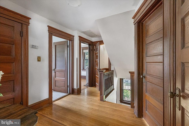 corridor with baseboards, an upstairs landing, and light wood-style flooring