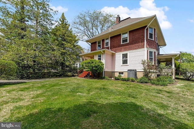back of property featuring a lawn, a chimney, and roof with shingles