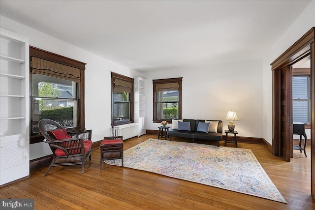 living room featuring built in features, a healthy amount of sunlight, wood finished floors, and radiator