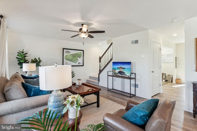 living area featuring ceiling fan, stairway, wood finished floors, and visible vents