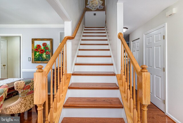 stairs with wood finished floors, ornamental molding, and baseboards