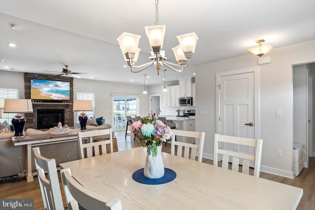 dining area with a fireplace, ceiling fan with notable chandelier, recessed lighting, baseboards, and wood finished floors