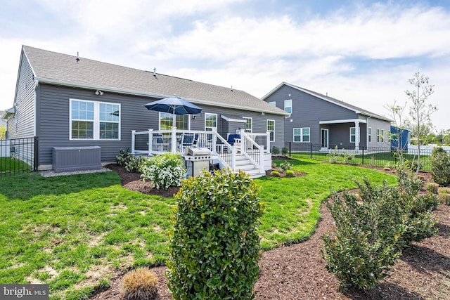 rear view of property with fence, a wooden deck, a shingled roof, and a lawn