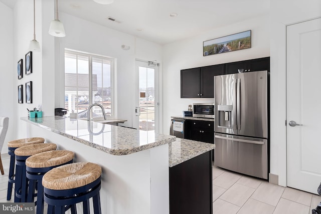 kitchen with visible vents, a peninsula, a breakfast bar, light stone counters, and appliances with stainless steel finishes