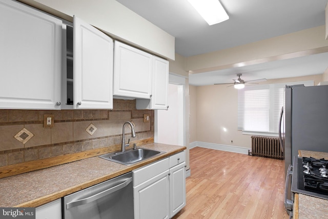 kitchen with stainless steel dishwasher, radiator heating unit, backsplash, a sink, and white cabinetry