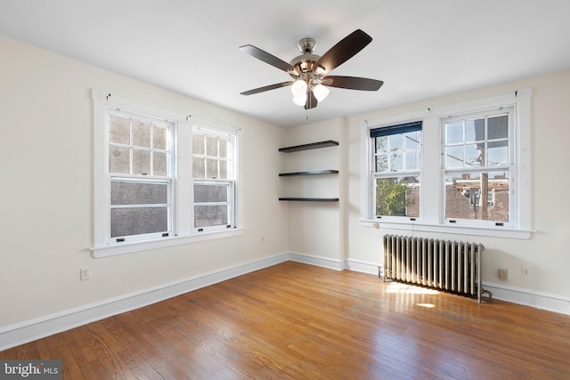 spare room with baseboards, radiator, a ceiling fan, and wood finished floors