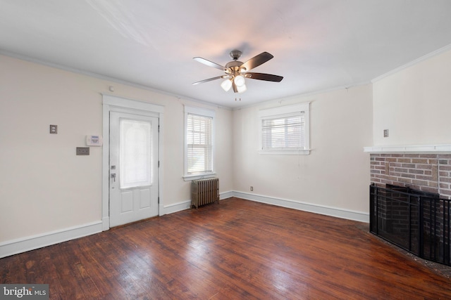 unfurnished living room with wood finished floors, radiator, ceiling fan, a brick fireplace, and crown molding