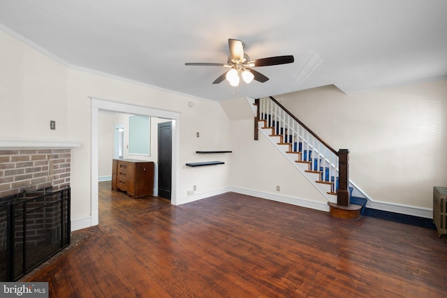 unfurnished living room featuring a brick fireplace, ceiling fan, stairs, ornamental molding, and wood finished floors