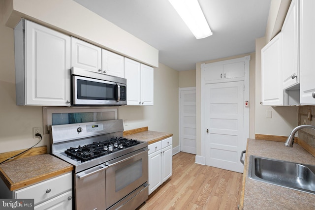 kitchen featuring white cabinetry, a sink, stainless steel appliances, light countertops, and light wood-type flooring