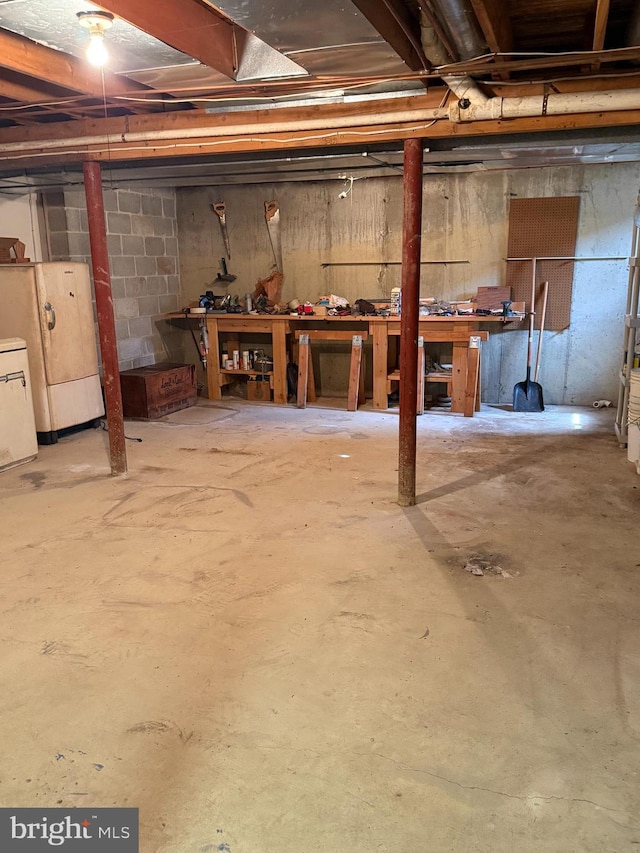 unfinished below grade area with a workshop area and freestanding refrigerator