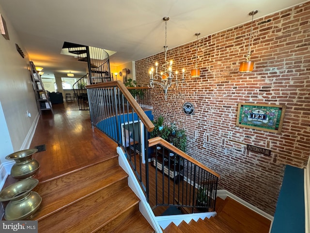 staircase with brick wall, baseboards, hardwood / wood-style floors, and a notable chandelier
