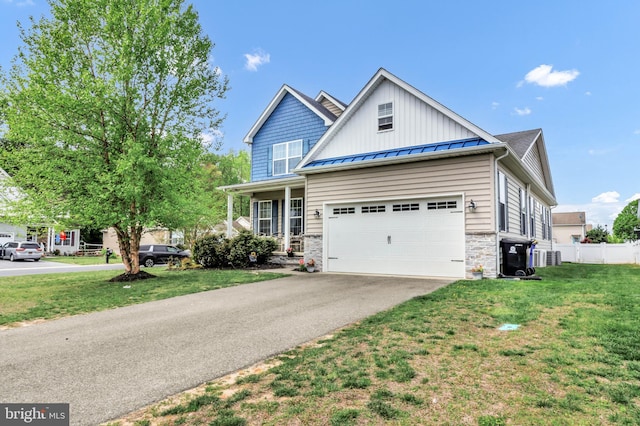 view of front of home featuring a standing seam roof, fence, aphalt driveway, stone siding, and a front lawn