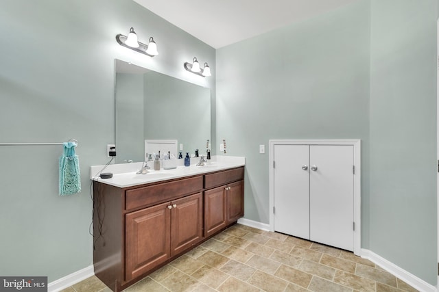 full bathroom with double vanity, a sink, and baseboards