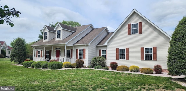 new england style home with roof with shingles, covered porch, and a front lawn