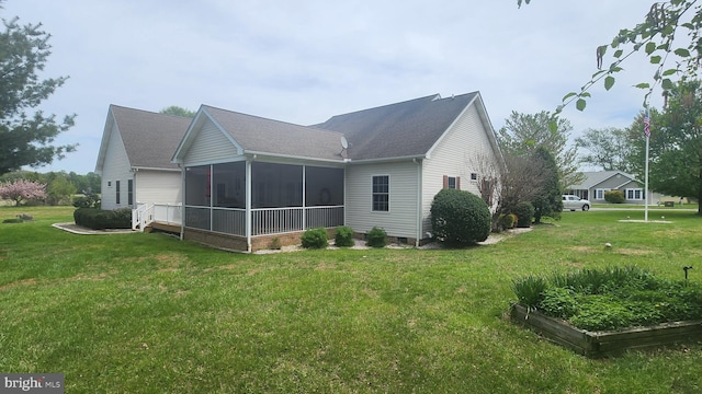 back of property with a yard, a vegetable garden, a sunroom, and roof with shingles