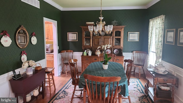 dining area with a chandelier, crown molding, visible vents, wallpapered walls, and wood finished floors