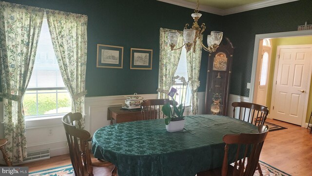 dining room featuring a wainscoted wall, a notable chandelier, ornamental molding, and wood finished floors