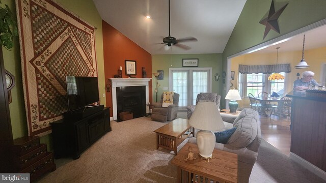 living room with high vaulted ceiling, a ceiling fan, a fireplace with flush hearth, and carpet flooring
