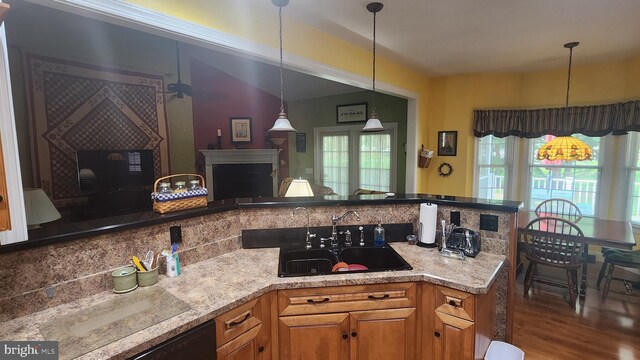 kitchen featuring a sink, a fireplace, brown cabinetry, backsplash, and pendant lighting