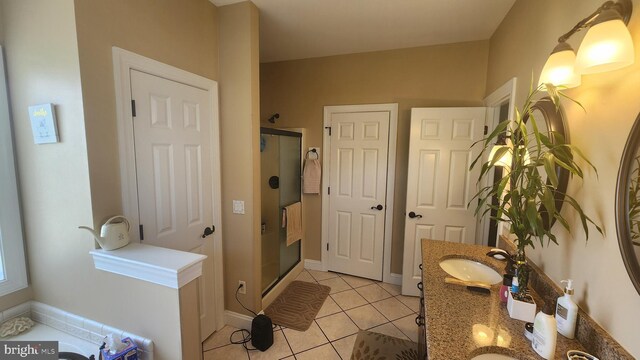 bathroom featuring a shower stall, a sink, double vanity, baseboards, and tile patterned floors