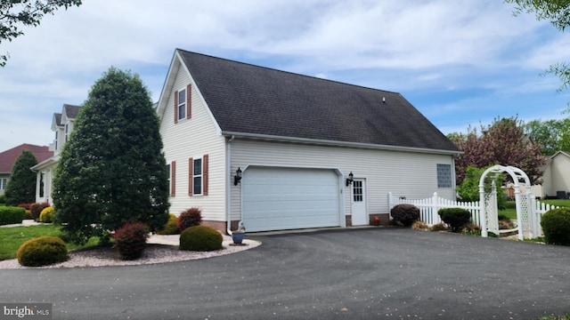 view of side of property with fence, aphalt driveway, a shingled roof, and a garage