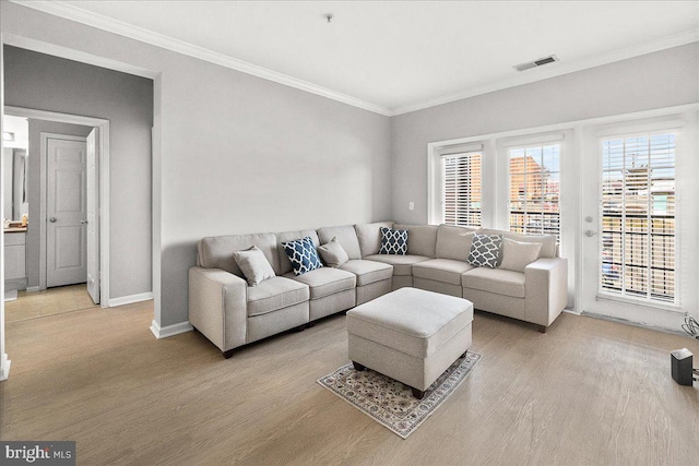 living room featuring ornamental molding, visible vents, light wood-style flooring, and baseboards