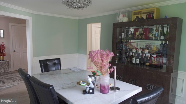 dining room featuring ornamental molding, wainscoting, wood finished floors, and a chandelier
