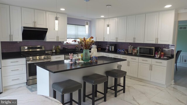 kitchen featuring tasteful backsplash, appliances with stainless steel finishes, marble finish floor, white cabinets, and a kitchen bar