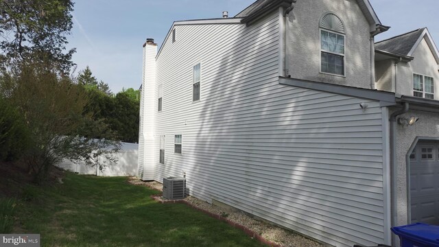 view of side of property with fence, a chimney, an attached garage, a lawn, and central AC unit
