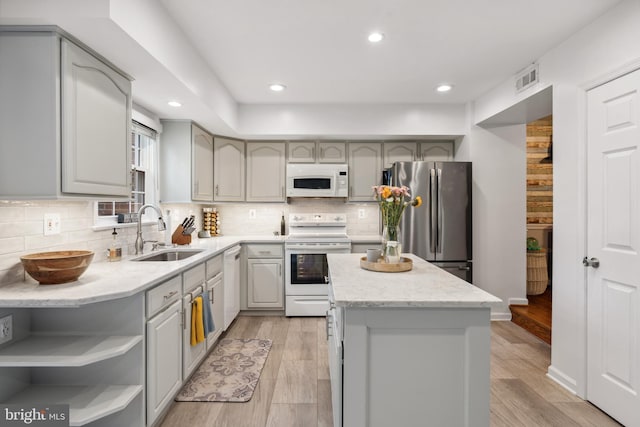 kitchen featuring white appliances, a sink, a kitchen island, decorative backsplash, and light wood-style flooring