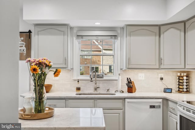 kitchen featuring white appliances, a sink, decorative backsplash, light stone countertops, and recessed lighting
