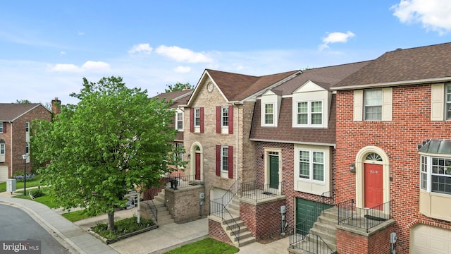 townhome / multi-family property with a garage, brick siding, a shingled roof, and a residential view