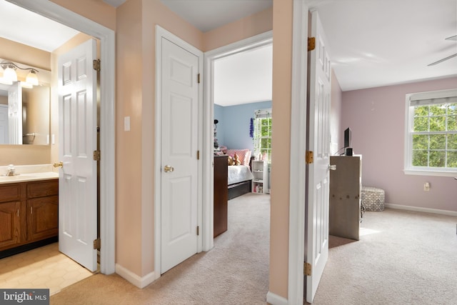 hallway with a sink, light carpet, and baseboards