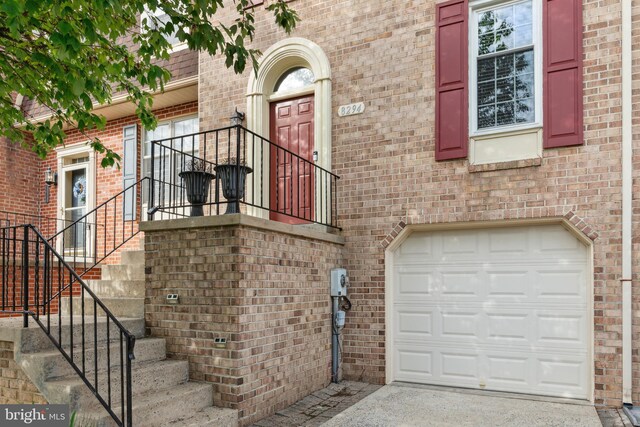 view of exterior entry with a garage, brick siding, and driveway