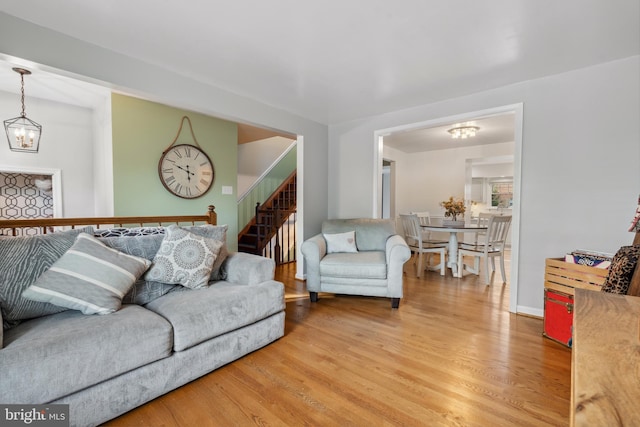 living area featuring a chandelier, light wood-style flooring, stairway, and baseboards