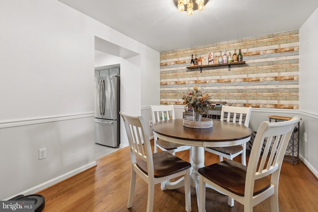 dining space featuring an accent wall, wooden walls, light wood-type flooring, and baseboards