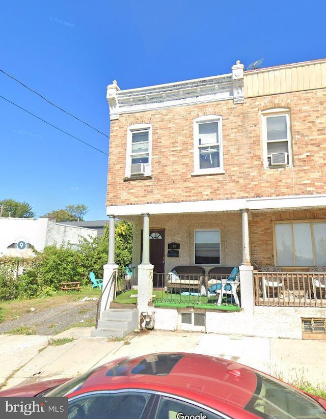 rear view of property with covered porch, brick siding, and cooling unit