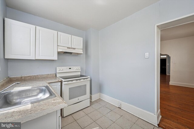 kitchen featuring a sink, under cabinet range hood, white electric range, white cabinetry, and baseboards